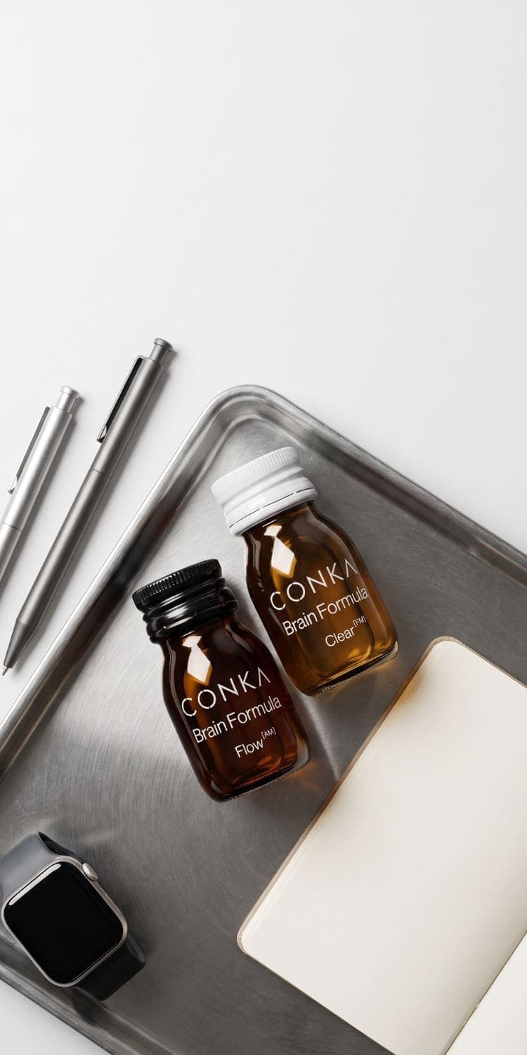 CONKA Flow and Clear shots on a steel desk tray beside a watch, pens and a notebook